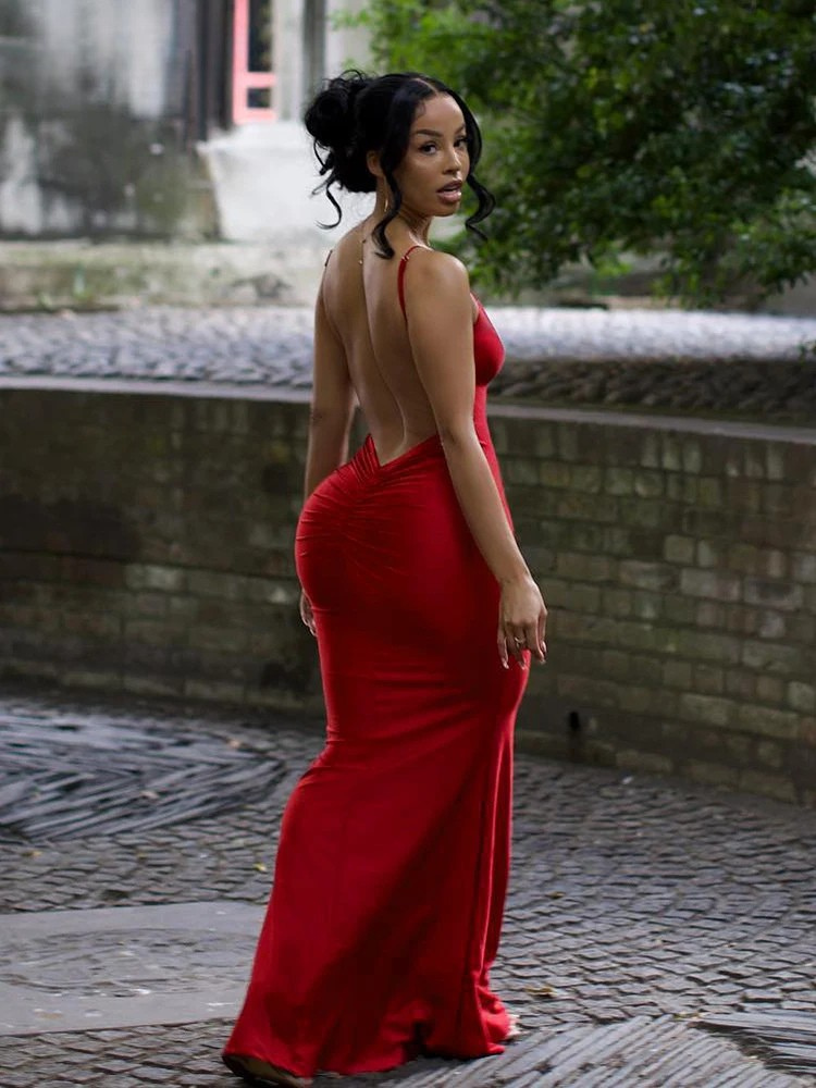 Woman in a red evening gown with an open back standing outdoors.