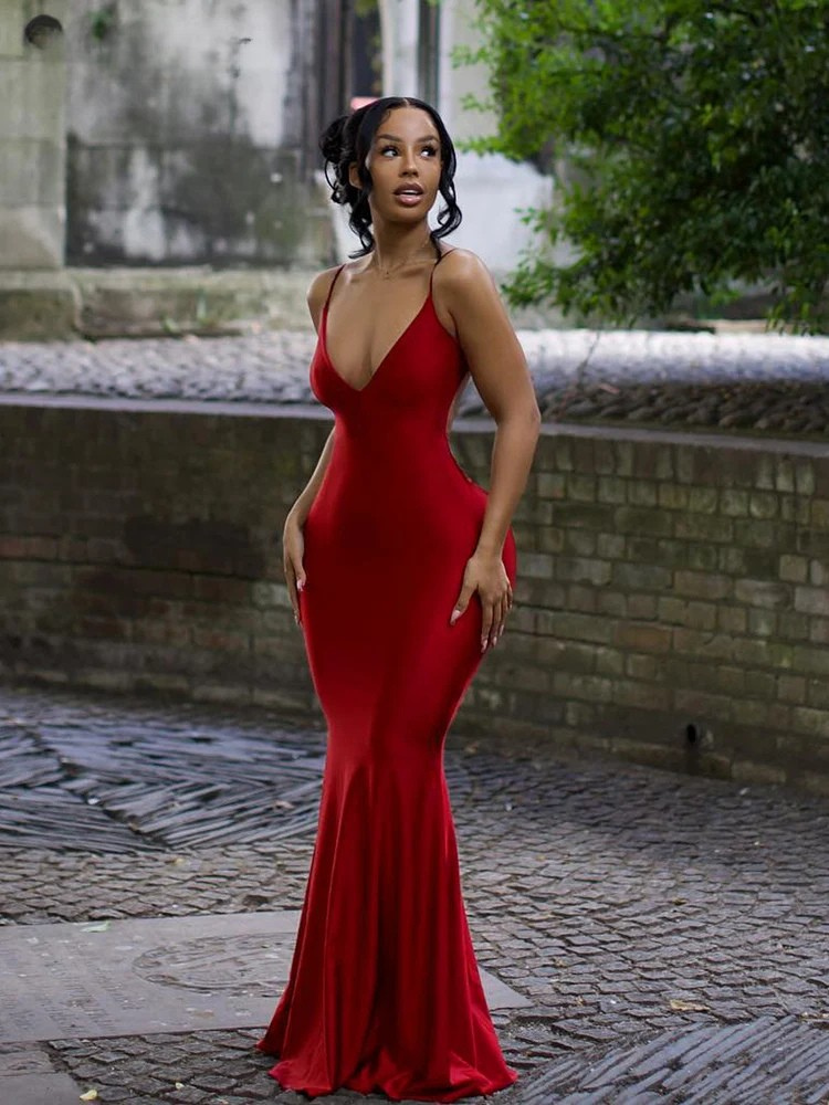 Woman in a red dress standing outdoors on a cobblestone street.