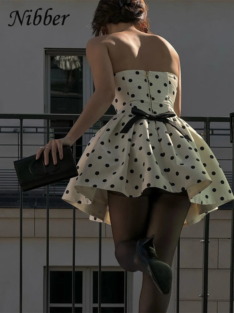 Woman wearing a polka dot dress with a black bow, standing on a balcony.