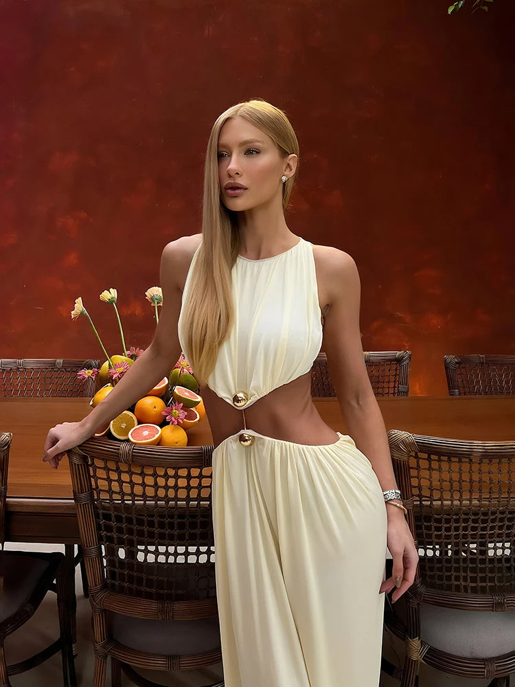 Woman in a white dress standing in a dining room with fruit and flowers on a table.