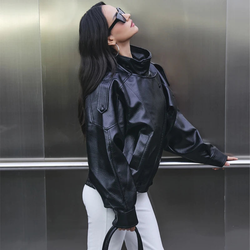 Person wearing a black leather jacket and sunglasses against a metallic wall.