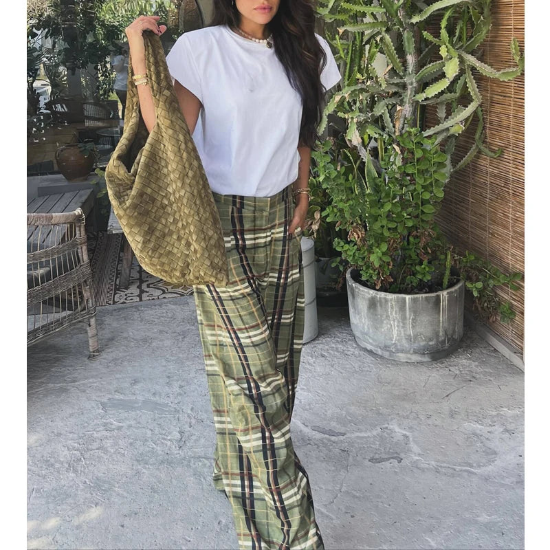 Person wearing a white top and green plaid pants holding a green bag outdoors.