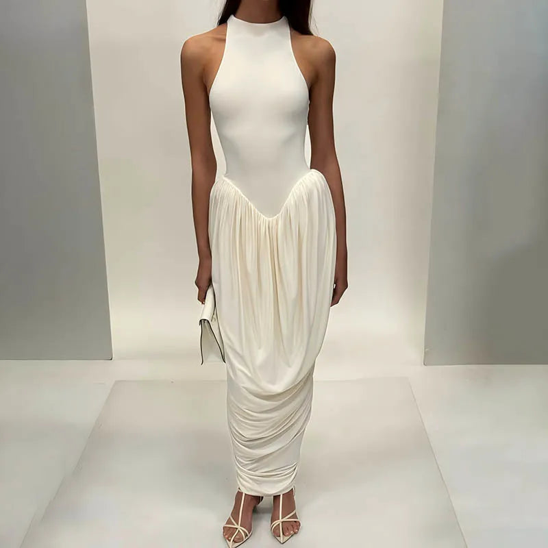 Woman wearing a white halter neck dress with a draped skirt on a plain background