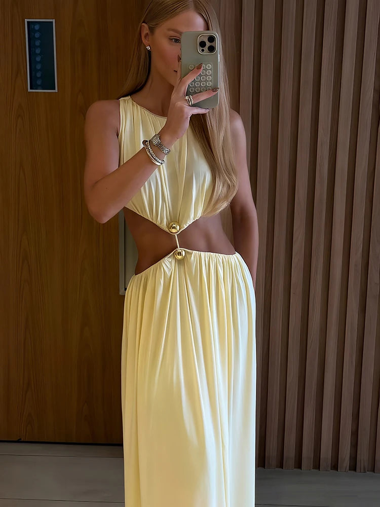 Woman wearing a yellow dress with cut-out design, standing in front of a wooden wall.