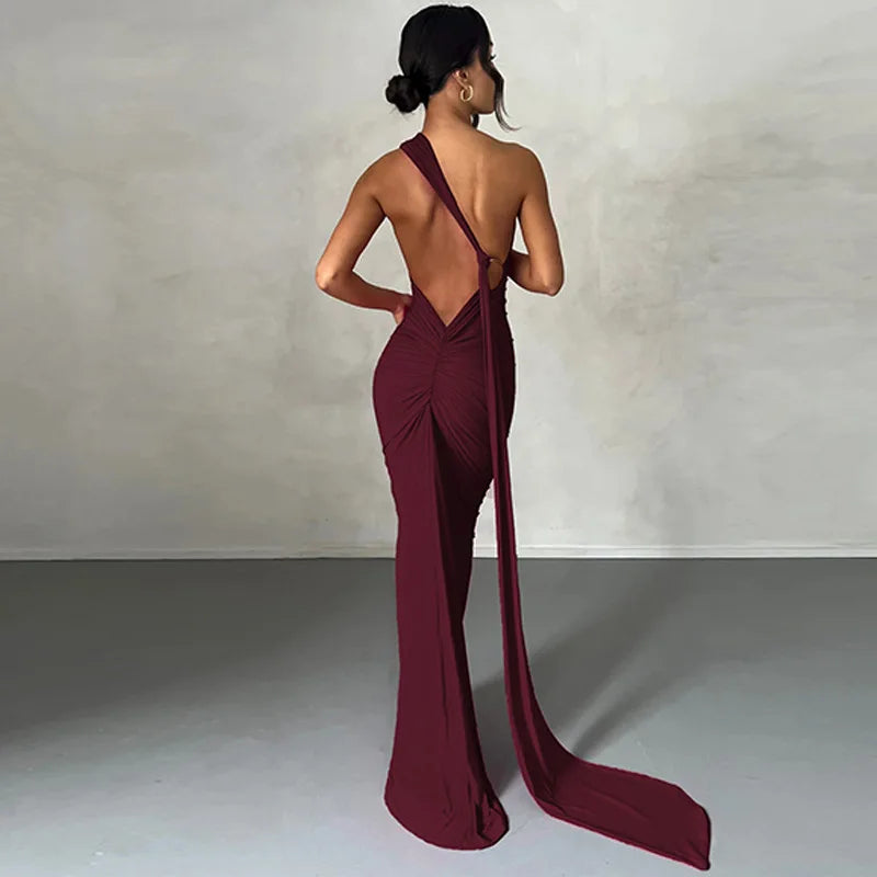 Woman wearing a burgundy evening gown with a high slit and open back against a plain background