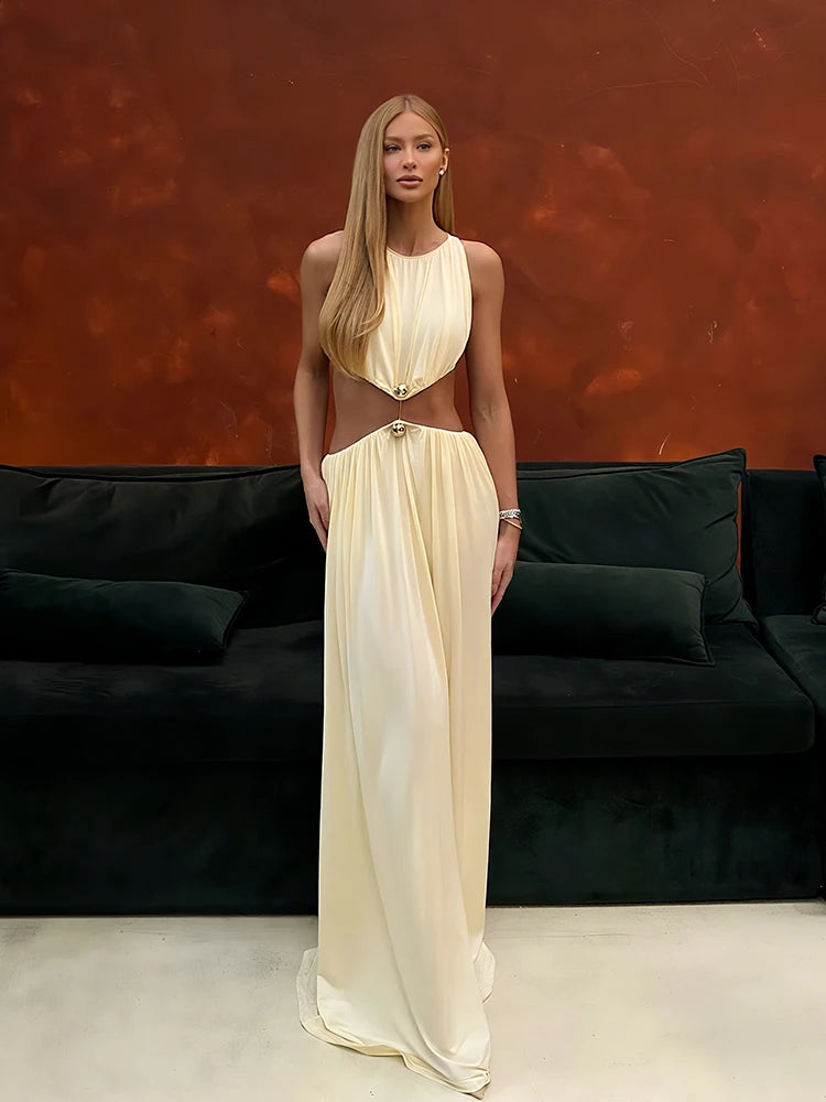 Woman in a long, flowing dress standing in front of a dark sofa with a red-brown abstract wall.