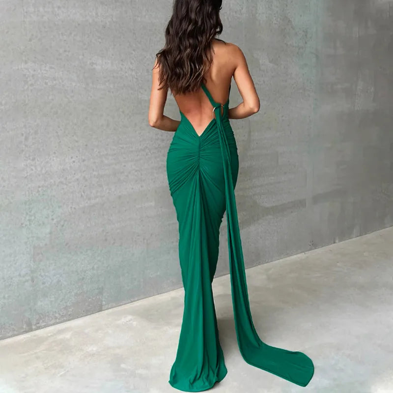 Woman wearing a green evening gown with a backless design against a gray wall.